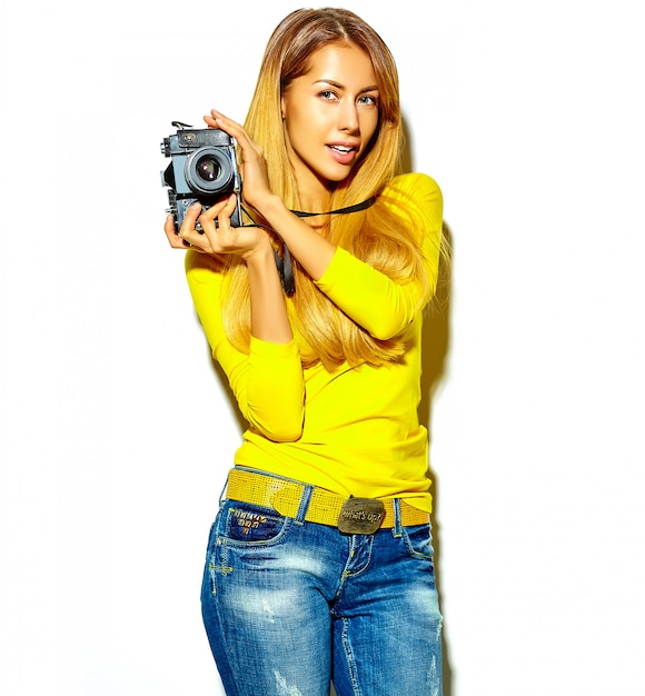 portrait of beautiful happy cute smiling blond woman girl in casual summer clothes takes photos holding retro photographic camera, isolated on a white