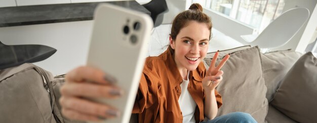 Free photo portrait of beautiful happy girl takes selfies on sofa woman posing for photos on her couch taking