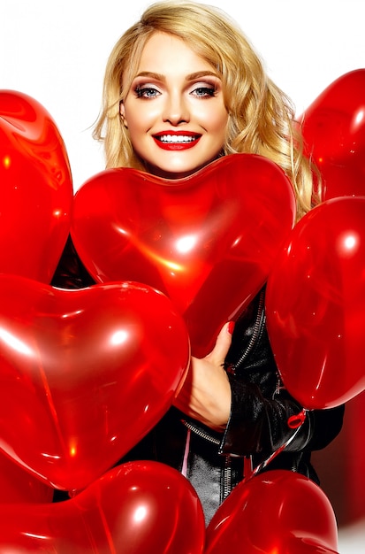 Портрет красивой счастливой сладкой улыбающейся блондинки девушка держит в руках красные сердечные воздушные шары в повседневной черной хипстерской одежде