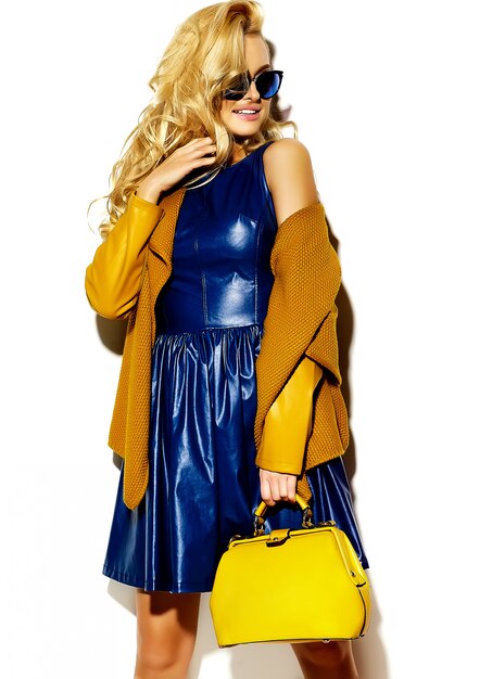 Портрет красивой счастливой сладкой улыбающейся блондинки женщины в повседневной хипстерской теплой зимней одежде свитера, с желтой сумочкой в солнцезащитных очках