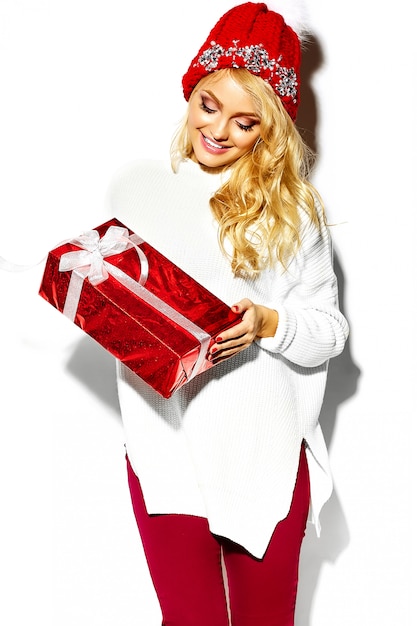 portrait of beautiful happy sweet smiling blonde woman woman holding in her hands big Christmas gift box in casual red hipster winter clothes, in white warm sweater