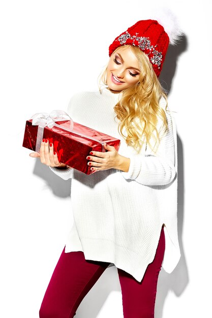 portrait of beautiful happy sweet smiling blonde woman woman holding in her hands big Christmas gift box in casual red hipster winter clothes, in white warm sweater