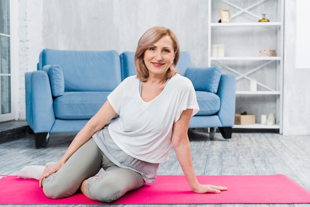 Free photo portrait of a beautiful happy woman sitting on pink yoga mat looking at camera
