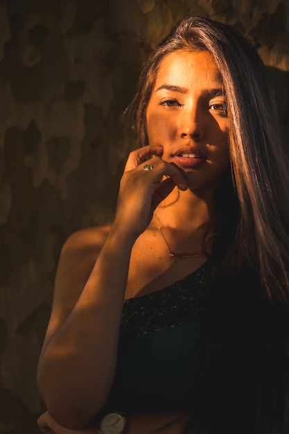 Portrait of a beautiful Hispanic female standing against a wall with the sunlight falling on her