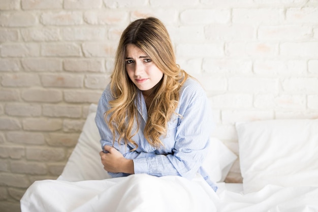Foto gratuita ritratto di una bella giovane donna ispanica in pigiama che si sente male con i pms mentre è seduta a letto