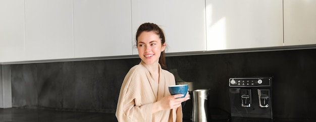 Free photo portrait of beautiful housewife young woman in bathrobe holding cup of coffee drinking tea in the