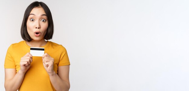 Portrait of beautiful korean girl holding credit card recommending bank service standing in yellow t...