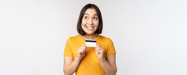 Portrait of beautiful korean girl holding credit card recommending bank service standing in yellow t