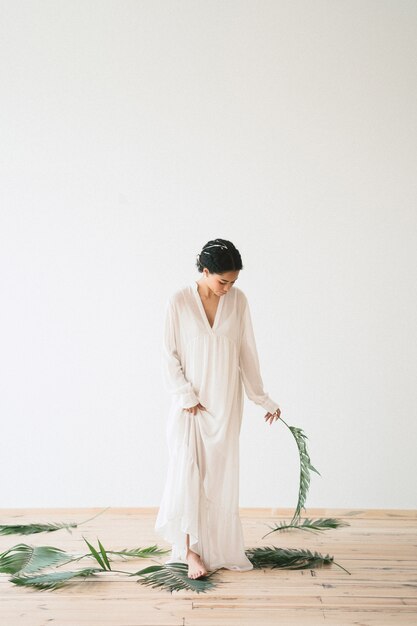 Портрет красивой леди в пустой комнате, стоя и держа пальмовая ветвь в длинном белом платье место для текста