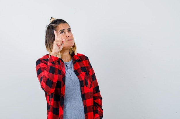 Portrait of beautiful lady pointing up, looking upward in casual clothes and looking confident front view