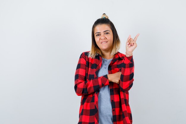 Portrait of beautiful lady pointing at upper right corner in casual clothes and looking cheery front view