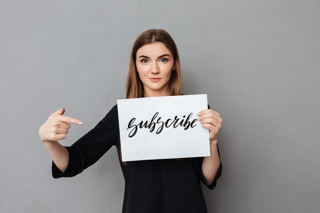 Portrait of beautiful lady standing and holding postcard while dreamily looking in camera on gray background