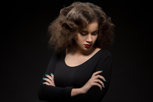 Portrait of beautiful lady with modern hairstyle posing with her arms crossed while looking downwards.