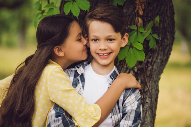 免费的肖像照片美丽的小女孩拥抱甜蜜的男孩和亲吻他的脸颊