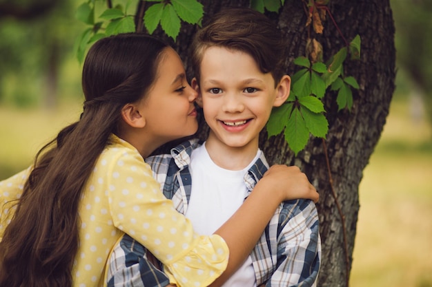 Portrait of beautiful little girl hugging sweet boy and kissing him on cheek