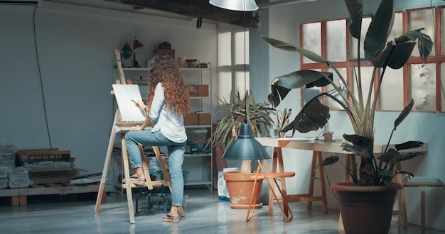 Free photo portrait of a beautiful longhaired female artist at work at her canvas in a studio