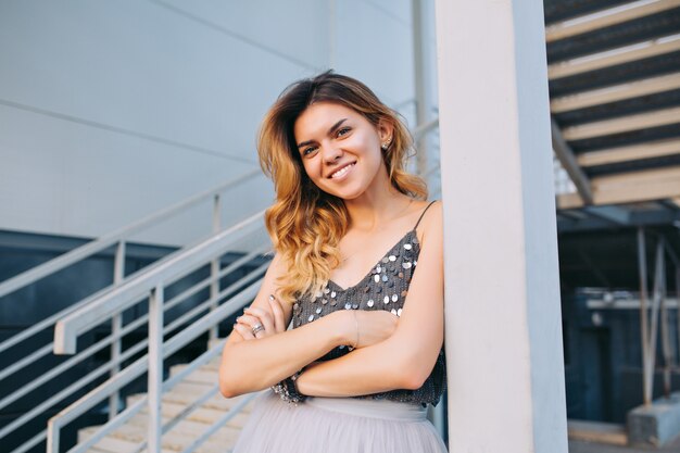 Portrait of beautiful model in grey shirt  leaning on pillar on stairs . She is smiling .