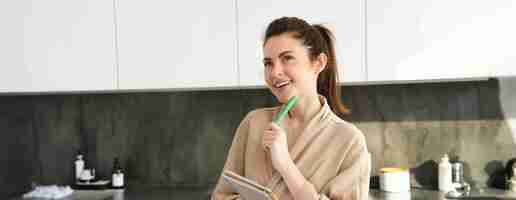 Free photo portrait of beautiful modern woman writing down grocery list meal ideas in notebook standing in the