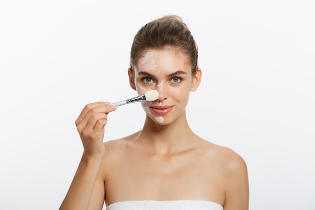 Portrait beautiful naked woman apply cosmetic white clay mask on with brush isolated on a white back