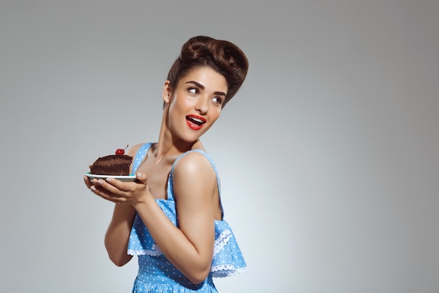 Portrait of beautiful pin-up woman holding cake in hands