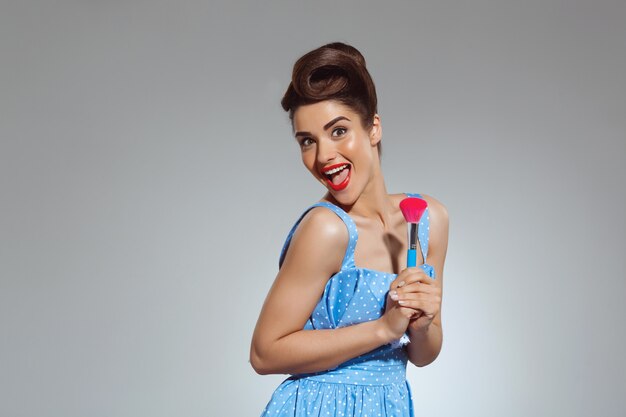 Portrait of beautiful pin-up woman at studio holding make-up brush