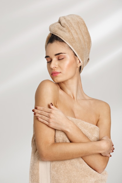 Ritratto di bella giovane donna sciccosa dopo la stazione termale che sta coperta in asciugamano.