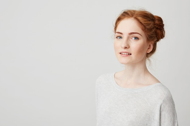 Portrait of beautiful redhead girl with buns and freckles smiling .