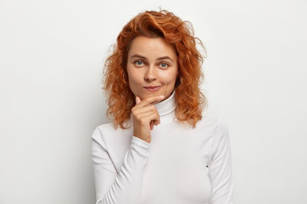 Portrait of beautiful redhead woman with natural look, touches chin and purses lips