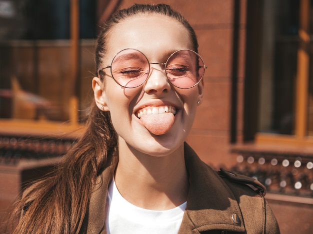그녀의 혀를 보여주는 여름 힙 스터 재킷 옷을 입고 아름다운 웃는 갈색 머리 모델의 초상화