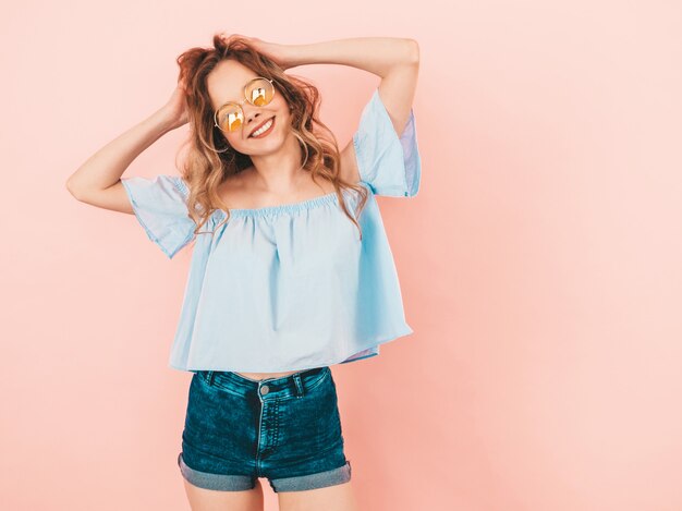 Portrait of beautiful smiling cute model in round sunglasses. Girl in summer colorful clothes. Model posing. Playing with her hair