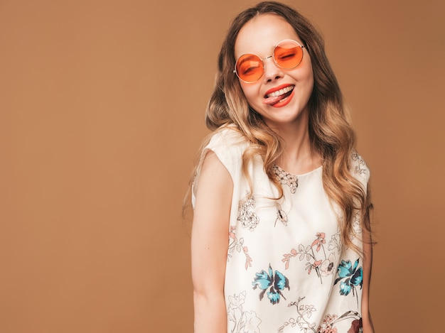 Portrait of beautiful smiling cute model with pink lips. Girl in summer colorful dress and sunglasses. Model posing