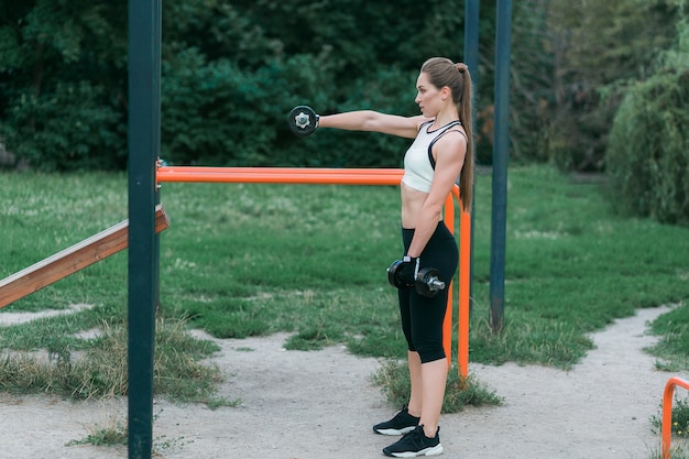 Foto gratuita ritratto di bella ragazza sorridente con manubri, allenamento all'aperto nel parco.