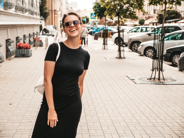 Portrait of beautiful smiling model dressed in summer clothes. Trendy girl posing in the street in sunglasses. Funny and positive woman having fun