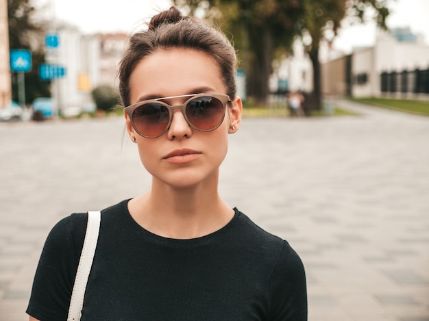 Portrait of beautiful smiling model dressed in summer clothes. Trendy girl posing in the street in sunglasses. Funny and positive woman having fun