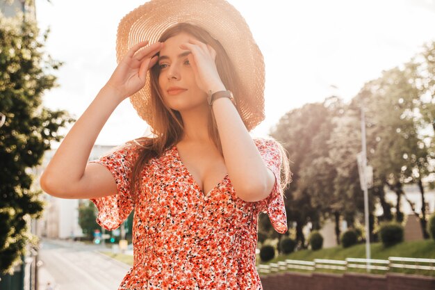 Portrait of beautiful smiling model dressed in summer hipster dress.Sexy carefree girl posing in the street background at sunset.Trendy funny and positive woman in hat