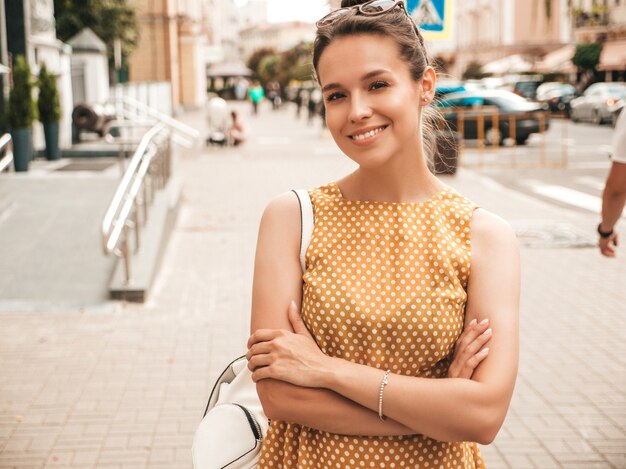 Портрет красивые улыбающиеся модели, одетые в летнее желтое платье. Модная девушка позирует на улице. Веселая и позитивная женщина с удовольствием