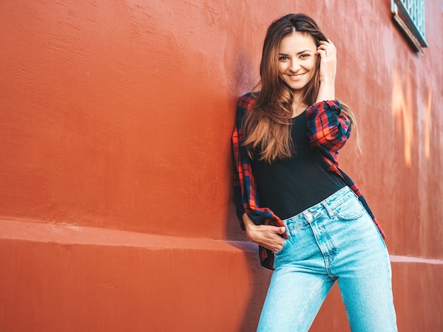 Portrait of beautiful smiling model. female dressed in summer hipster checkered shirt and jeans. she posing near wall in the street