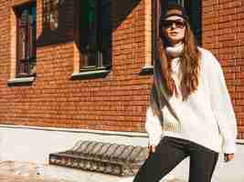 Foto gratuita ritratto di bella modella sorridente. donna vestita di caldo maglione bianco hipster e berretto. ragazza alla moda in posa per strada