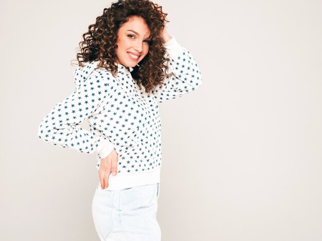 Portrait of beautiful smiling model with afro curls hairstyle dressed in summer hipster clothes.Sexy carefree girl posing on gray backgroundl.Trendy funny and positive woman in white hoodie