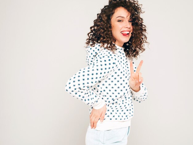 Portrait of beautiful smiling model with afro curls hairstyle dressed in summer hipster clothes.Sexy carefree girl posing on gray backgroundl.Trendy funny and positive woman in white hoodie