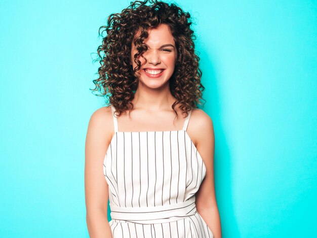 Portrait of beautiful smiling model with afro curls hairstyle dressed in summer hipster clothes.Sexy carefree girl posing near blue wall.Trendy funny and positive woman