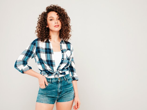 Portrait of beautiful smiling model with afro curls hairstyle dressed in summer hipster clothes.Sexy carefree girl posing in studio on gray background.Trendy funny and positive woman