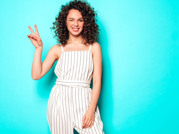 Portrait of beautiful smiling model with afro curls hairstyle dressed in summer hipster clothes.Trendy funny and positive woman shows peace sign