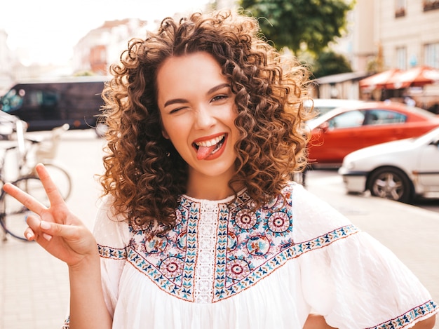 Foto gratuita il ritratto di bello modello sorridente con l'acconciatura dei riccioli di afro si è vestito in vestito bianco dai pantaloni a vita bassa dell'estate.