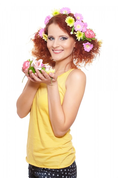 Portrait of beautiful smiling redhead ginger woman in yellow cloth with yellow pink colorful flowers in hair isolated on white holding flowers