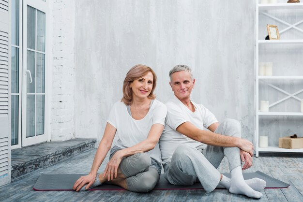 Портрет красивой улыбающейся старшей пары, сидящей на циновке йоги дома