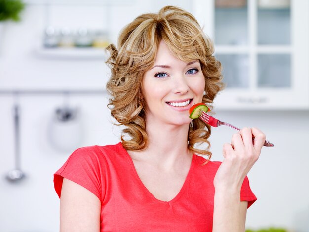 Портрет красивой улыбающейся женщины, едящей салат на кухне