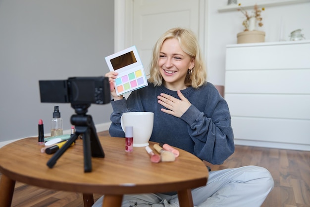 Free photo portrait of beautiful smiling woman recording video in her room has camera on coffee table reviewing