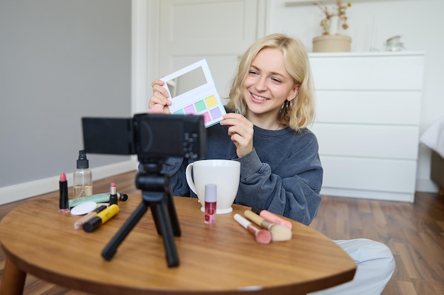 Free photo portrait of beautiful smiling woman recording video in her room has camera on coffee table reviewing