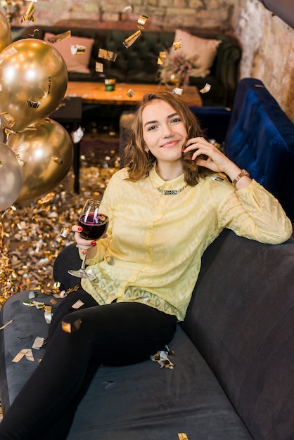 Portrait of a beautiful smiling woman sitting on sofa with glass of wine